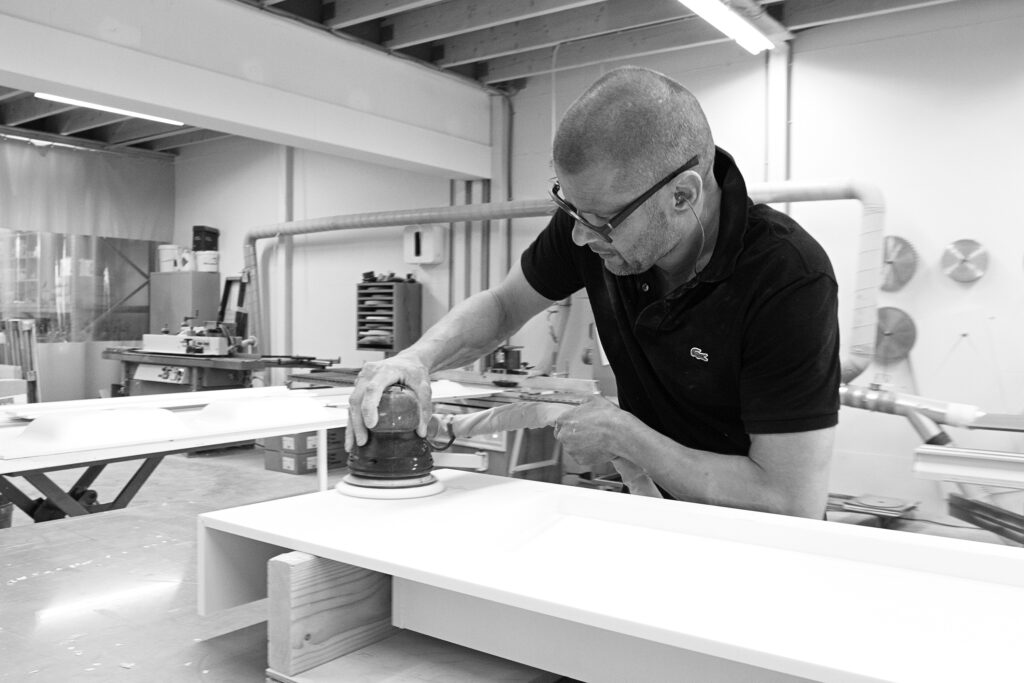 Medewerker schuurt in de werkplaats de rand van een wit Solid Surface wastafelblad met een excentrische schuurmachine