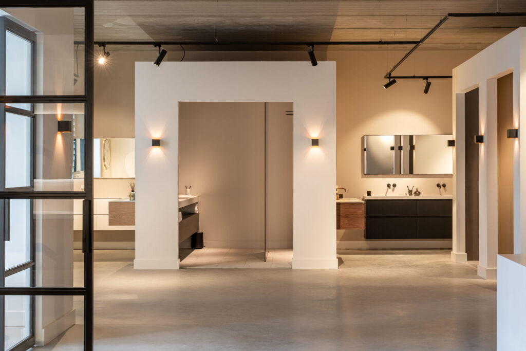 Showroom met verlichte wanden en spots, waarin verschillende badkamermeubels met wastafel staan opgesteld op een betonvloer